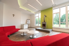 Das Foyer des Seminarhauses ©BDKJ Jugendhof Ein halbrundes, rotes Sofa im Vordergrund, ein Kamin vor einer Fensterfront im Hintergrund