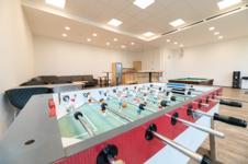 Der Freizeitraum mit Kicker und Sitzmöglichkeiten ©BDKJ Jugendhof Kicker im Vordergrund, Sofas, Tische, Stühle und eine Küchenzeile im Hintergrund